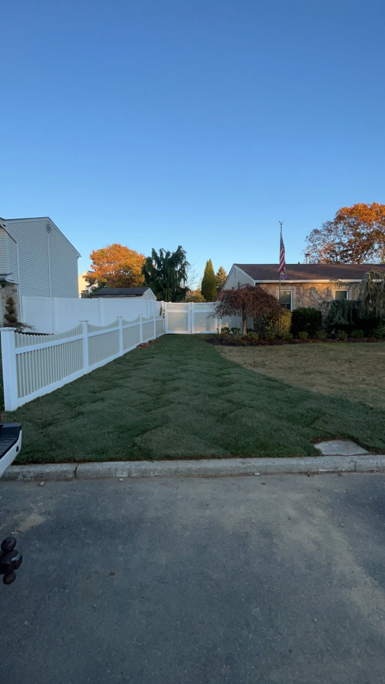 Freshly laid sod covers a suburban front yard with a white fence and houses beneath a blue sky.